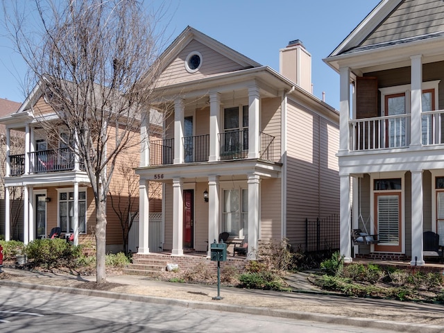 greek revival house with a balcony, brick siding, and covered porch