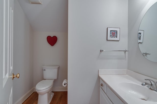 half bath with vanity, wood finished floors, visible vents, baseboards, and toilet