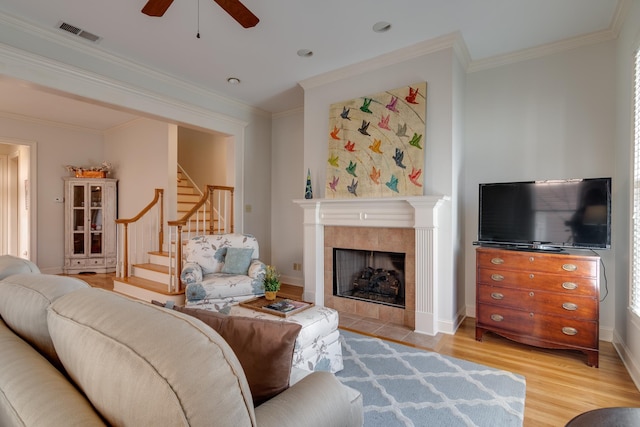 living area with visible vents, a tiled fireplace, stairs, ornamental molding, and light wood-style flooring