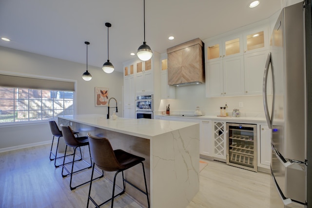 kitchen featuring beverage cooler, premium range hood, light wood finished floors, stainless steel appliances, and white cabinets