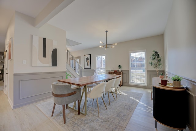 dining space with stairway, light wood-style floors, a wainscoted wall, and a notable chandelier