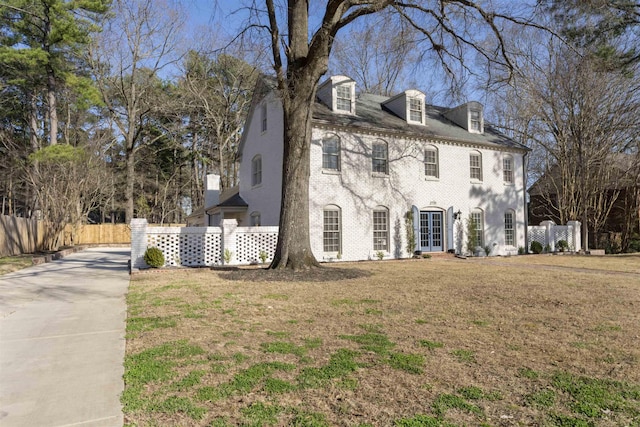 colonial inspired home with french doors, brick siding, a front lawn, and fence