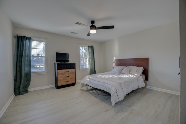 bedroom with light wood finished floors, visible vents, a ceiling fan, and baseboards