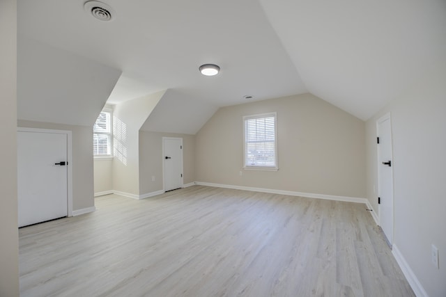 additional living space featuring vaulted ceiling, light wood-style floors, visible vents, and baseboards