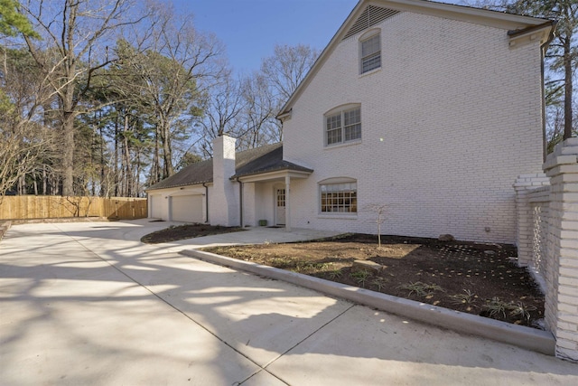 exterior space with driveway, fence, a garage, brick siding, and a chimney