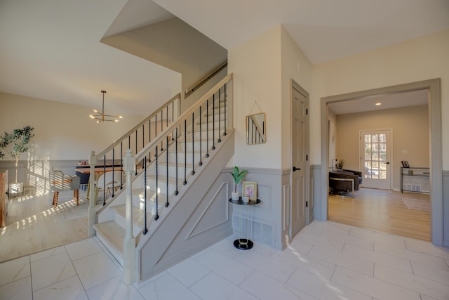 staircase featuring a notable chandelier, a wainscoted wall, a decorative wall, and wood finished floors