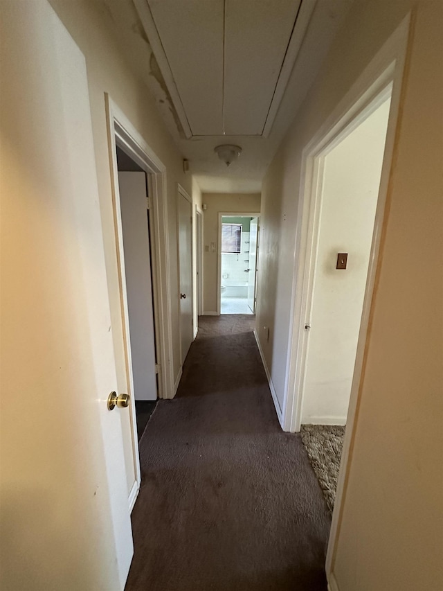 corridor featuring attic access and dark colored carpet