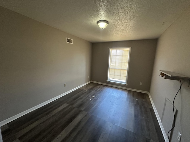 spare room featuring visible vents, a textured ceiling, dark wood-type flooring, and baseboards