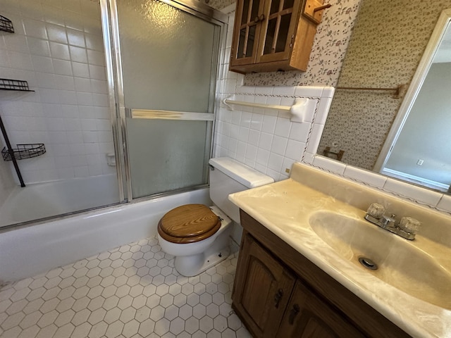 bathroom featuring toilet, combined bath / shower with glass door, tile walls, wallpapered walls, and vanity