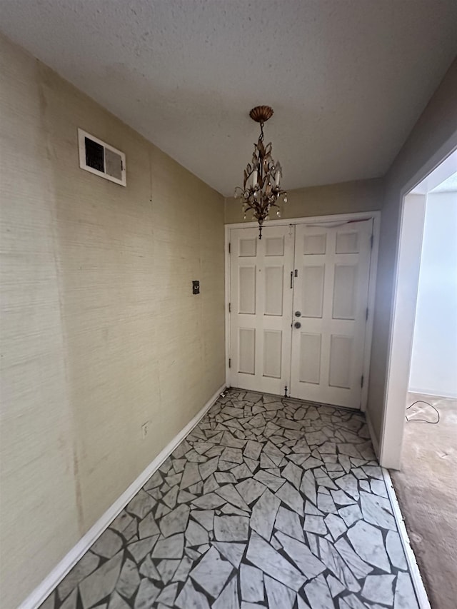 foyer entrance with a textured ceiling, baseboards, visible vents, and a chandelier