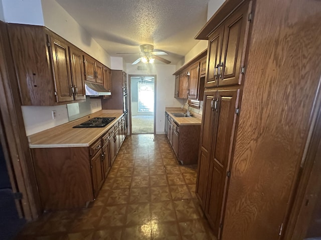 kitchen with a sink, stovetop, under cabinet range hood, and light countertops