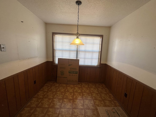 unfurnished dining area featuring wooden walls, wainscoting, and a textured ceiling