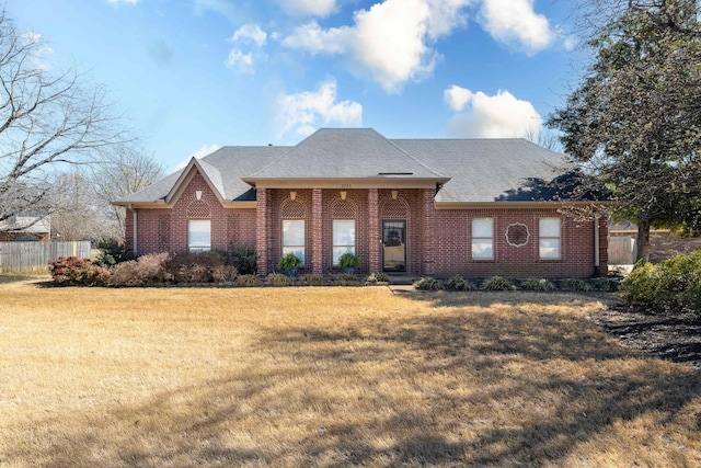 view of front of house with a front lawn, fence, brick siding, and a shingled roof