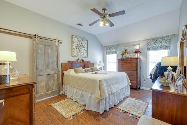 bedroom with baseboards, visible vents, hardwood / wood-style flooring, vaulted ceiling, and a barn door