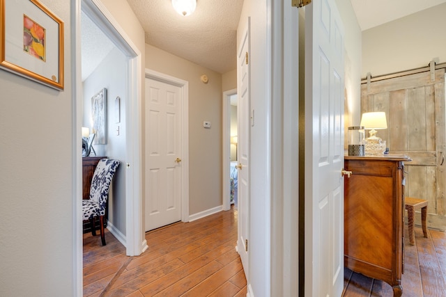 hall with baseboards, a textured ceiling, a barn door, and wood finished floors