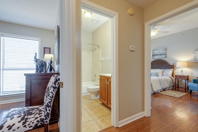 bedroom with baseboards, a textured ceiling, ensuite bath, and light wood-style flooring