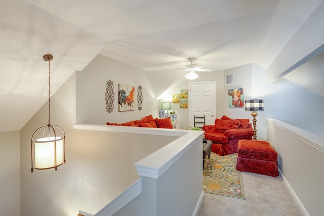 corridor featuring visible vents, an upstairs landing, a textured ceiling, carpet floors, and baseboards