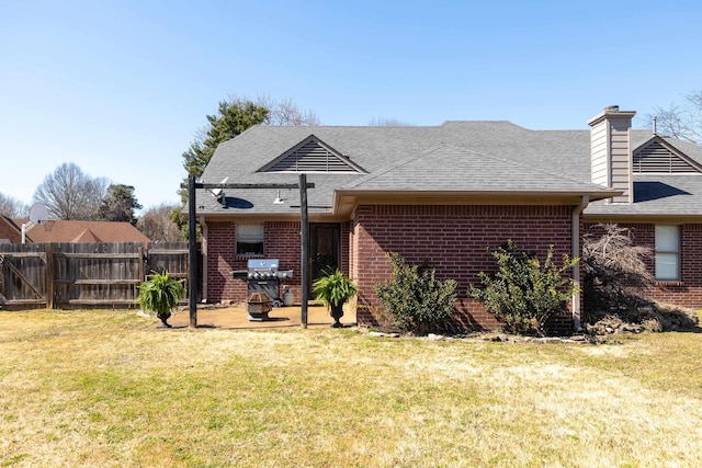 back of property featuring brick siding, a lawn, roof with shingles, and fence