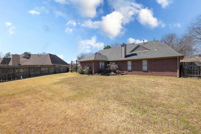 rear view of house with a yard, fence, brick siding, and a chimney