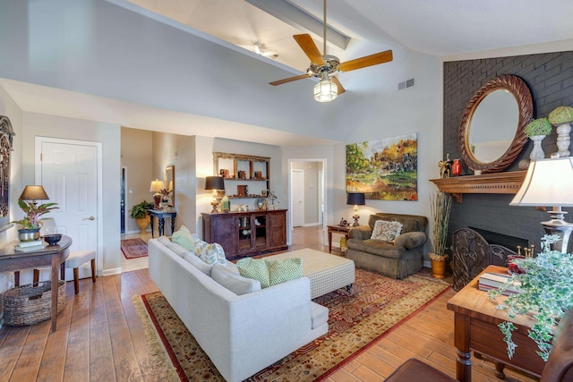 living area featuring a brick fireplace, visible vents, wood-type flooring, and high vaulted ceiling