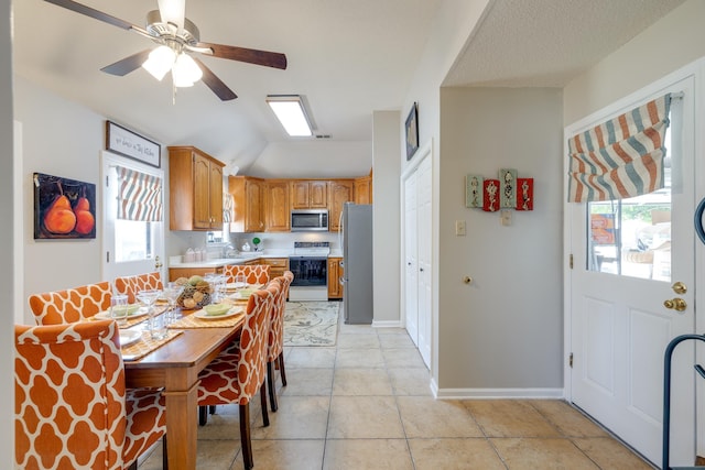 kitchen with a sink, stainless steel appliances, brown cabinetry, light countertops, and light tile patterned floors