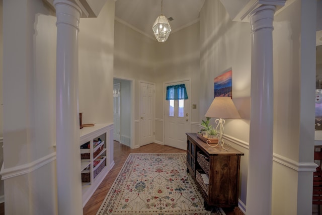 entrance foyer featuring a high ceiling, wood finished floors, ornate columns, and ornamental molding