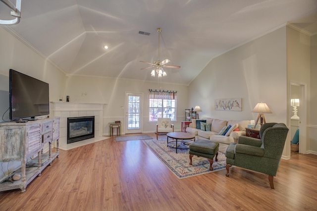 living room with light wood-type flooring, visible vents, a tile fireplace, and ornamental molding