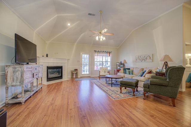 living room featuring visible vents, light wood finished floors, high vaulted ceiling, a tile fireplace, and crown molding