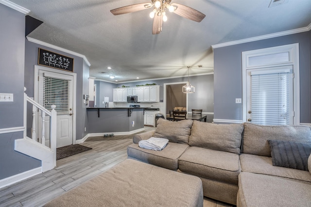 living area with crown molding, ceiling fan, baseboards, light wood-type flooring, and a textured ceiling