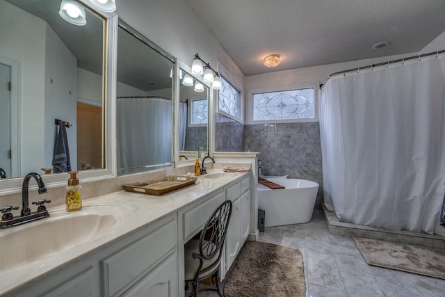 full bath featuring a textured ceiling, double vanity, a freestanding tub, and a sink