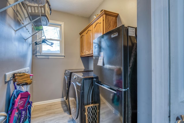 laundry area featuring baseboards, washer and clothes dryer, light wood-style flooring, cabinet space, and a textured ceiling