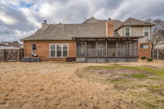 rear view of house featuring fence, brick siding, a chimney, and a sunroom