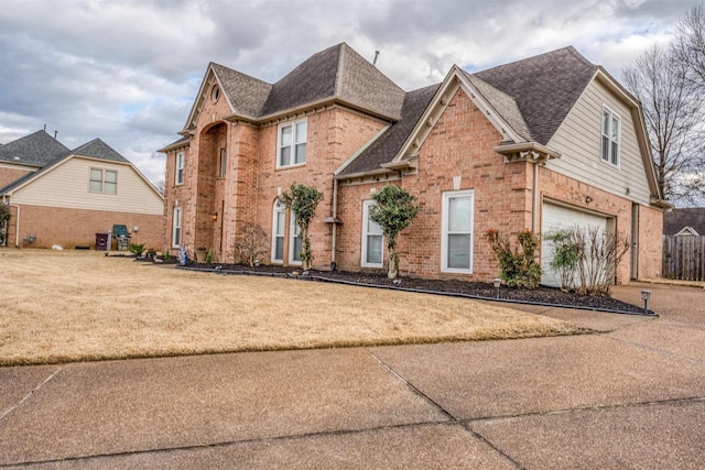 view of front of property with driveway, roof with shingles, an attached garage, a front lawn, and brick siding