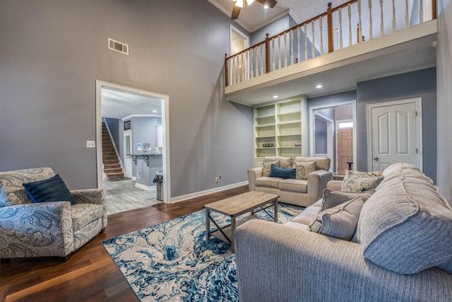 living area featuring built in shelves, wood finished floors, baseboards, visible vents, and ornamental molding