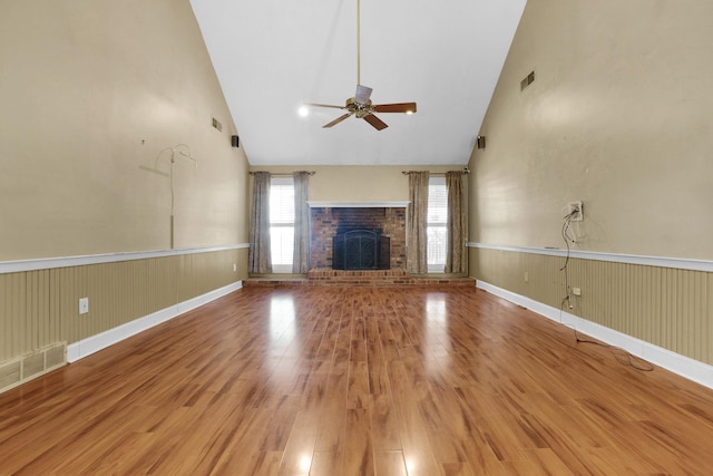 unfurnished living room with visible vents, a wainscoted wall, a fireplace, wood finished floors, and high vaulted ceiling