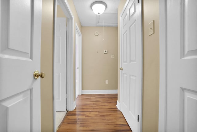 hall with a textured ceiling, attic access, baseboards, and wood finished floors