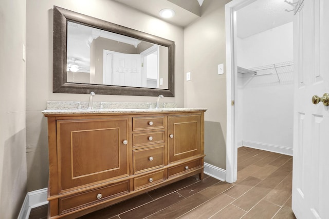 full bath with double vanity, wood finished floors, baseboards, and a sink