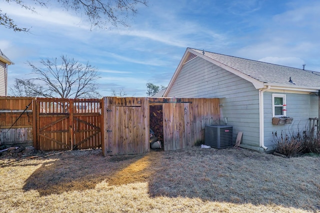 view of home's exterior with fence, central AC unit, a shingled roof, and a gate