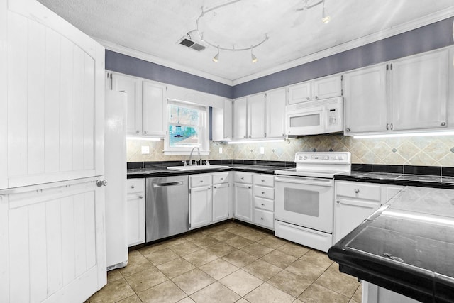 kitchen with white appliances, white cabinets, dark countertops, and a sink