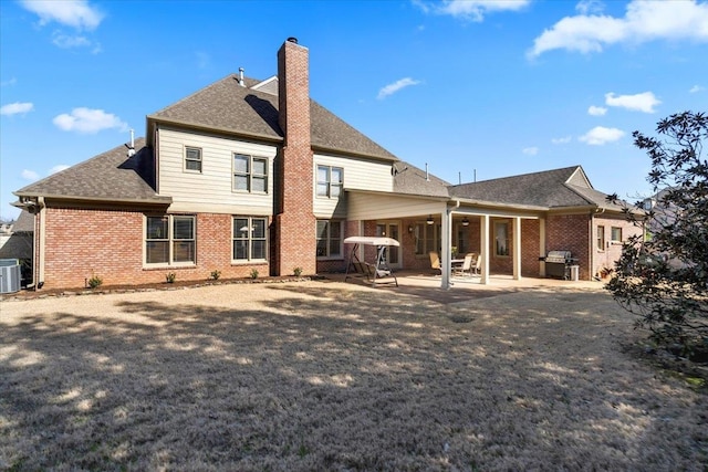 rear view of property with brick siding, central AC, roof with shingles, a chimney, and a patio area