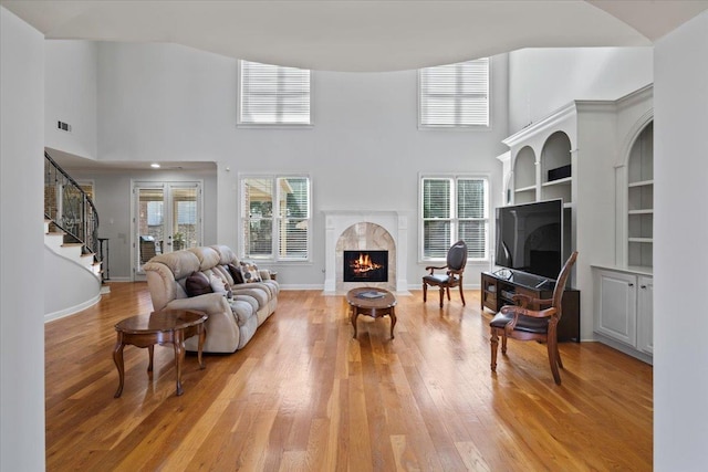 living area with a wealth of natural light, a fireplace, light wood-type flooring, and stairs