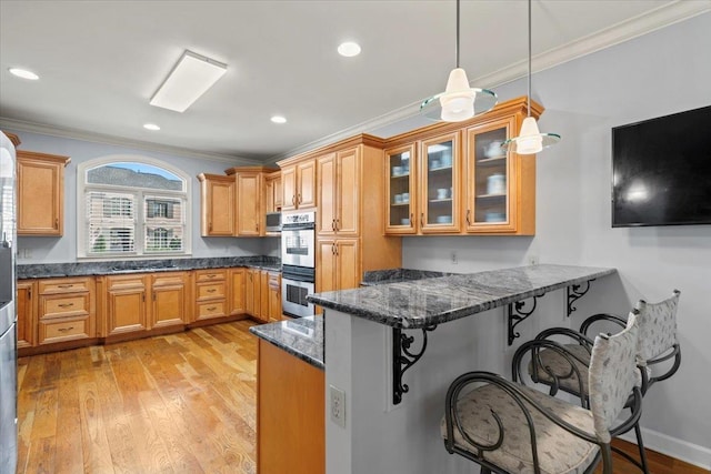 kitchen with dark stone counters, light wood-style floors, a peninsula, a breakfast bar area, and crown molding