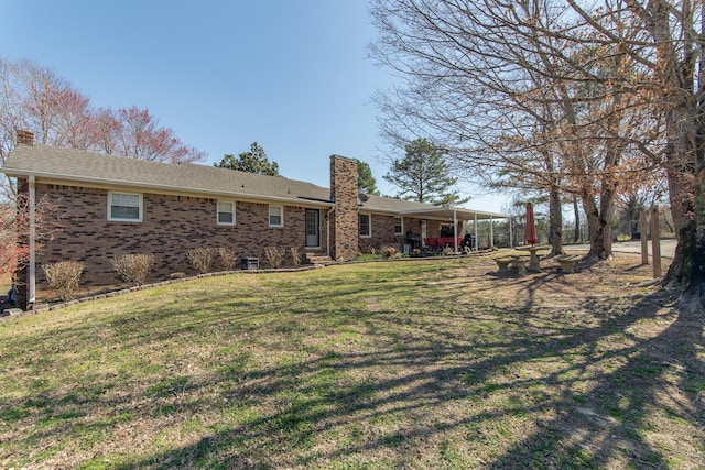 back of house with brick siding, a chimney, and a yard