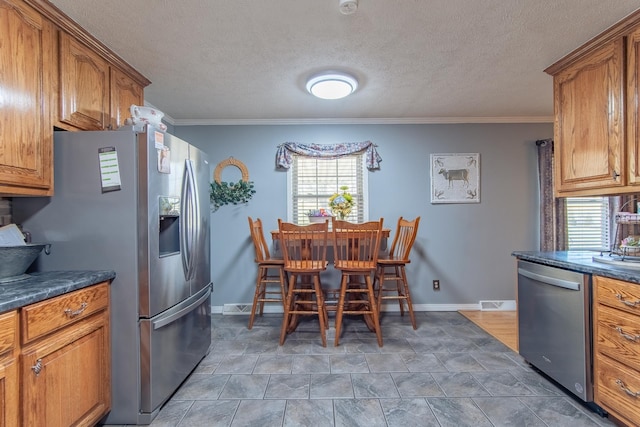 kitchen with brown cabinets, dark countertops, a textured ceiling, stainless steel appliances, and crown molding