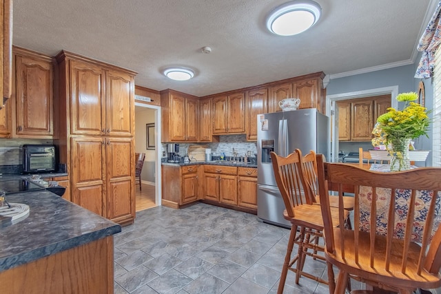 kitchen featuring brown cabinets, stainless steel fridge with ice dispenser, crown molding, dark countertops, and tasteful backsplash