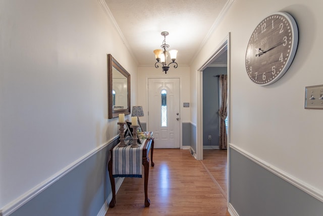 foyer with a textured ceiling, light wood-style flooring, a notable chandelier, and ornamental molding