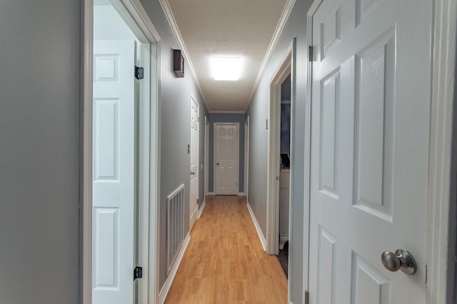 hall featuring visible vents, baseboards, light wood-style floors, and ornamental molding