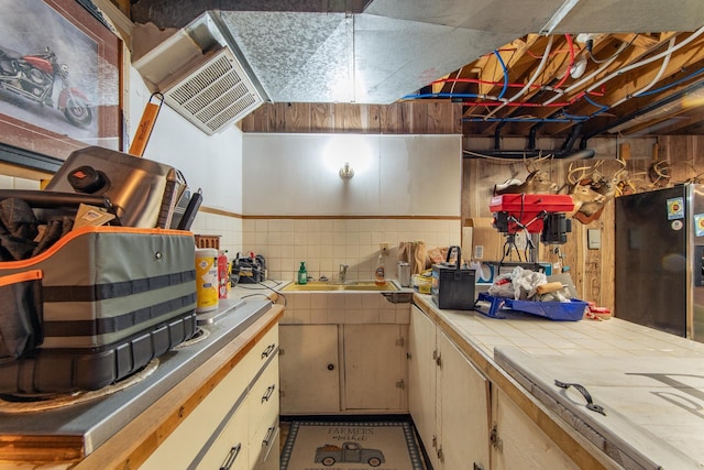 kitchen featuring decorative backsplash, tile countertops, freestanding refrigerator, and a sink