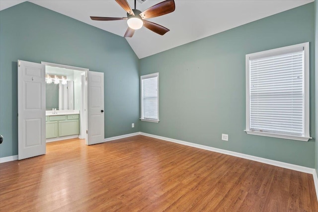 unfurnished bedroom featuring baseboards, lofted ceiling, ensuite bathroom, light wood-style floors, and a sink