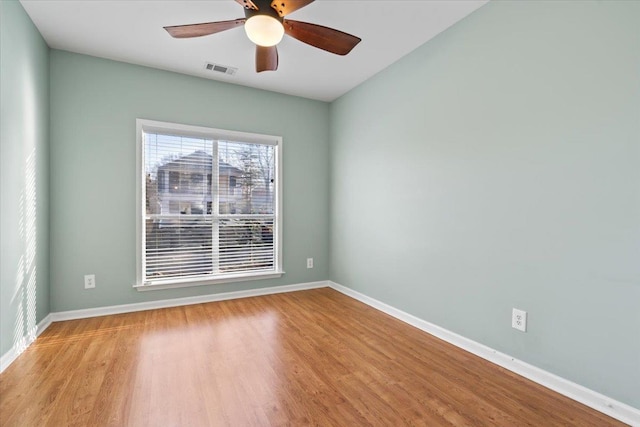 spare room with a ceiling fan, visible vents, wood finished floors, and baseboards